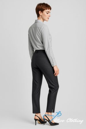 Full-length back view of a woman in a light gray shirt and dark tailored pants, wearing black heeled sandals in a studio setting.