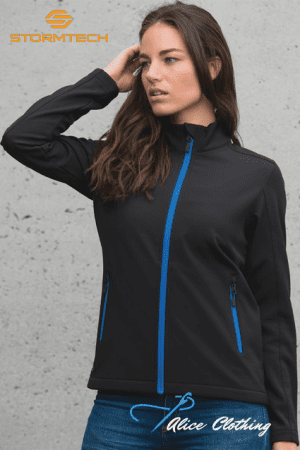 Woman wearing a black zip-up jacket with blue zipper accents, standing against a concrete wall; Stormtech and Alice Clothing logos visible above and at bottom right.