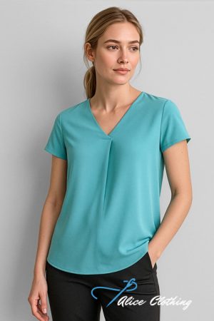 Woman wearing teal V-neck short-sleeve blouse, standing with one hand in pocket, against a light gray background.