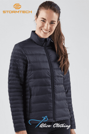 Smiling woman wearing a navy quilted Stormtech puffer jacket; Stormtech logo top left and Alice Clothing logo bottom.