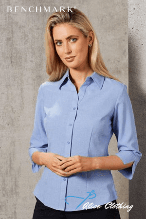 Model wearing a light-blue button-down shirt with 3/4 sleeves, standing against a concrete backdrop with subtle branding.