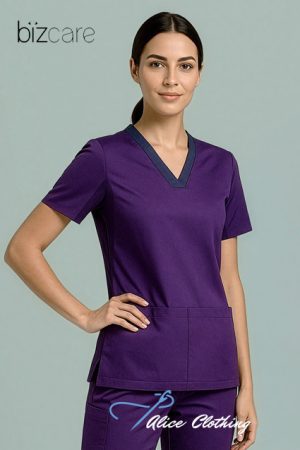 Female model wearing purple medical scrubs with dark V-neck trim, standing with hand on hip.