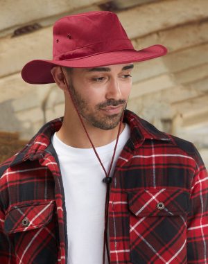 Man wearing a red wide-brim hat with a chin strap, red plaid flannel shirt, and white tee, looking downward.