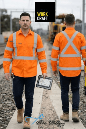Two construction workers in orange hi-vis jackets walk along a railway track; one faces the camera holding a tablet case/certificate holder.