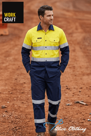 Man in a yellow and navy high-visibility work jumpsuit with reflective stripes stands on a dirt construction site.