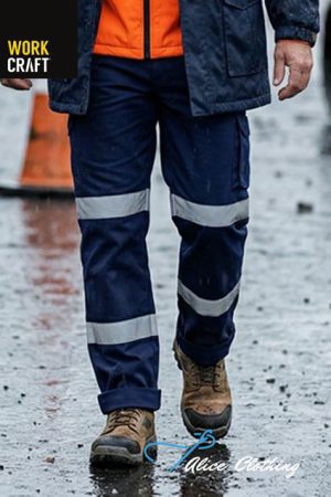 Worker wearing navy cargo pants with reflective bands and brown boots on a wet street; orange jacket visible with Work Craft and Alice Clothing logos.