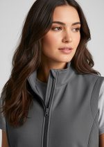 Woman with long brown hair wearing a gray zip-front vest, looking to the side in a neutral studio setting.