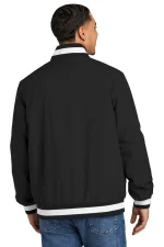 Back view of a man wearing a black varsity-style jacket with white striped collar and hem, blue jeans visible from the back.