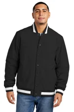 Front view of a man modeling a black varsity jacket with white trim on the collar, cuffs, and hem.