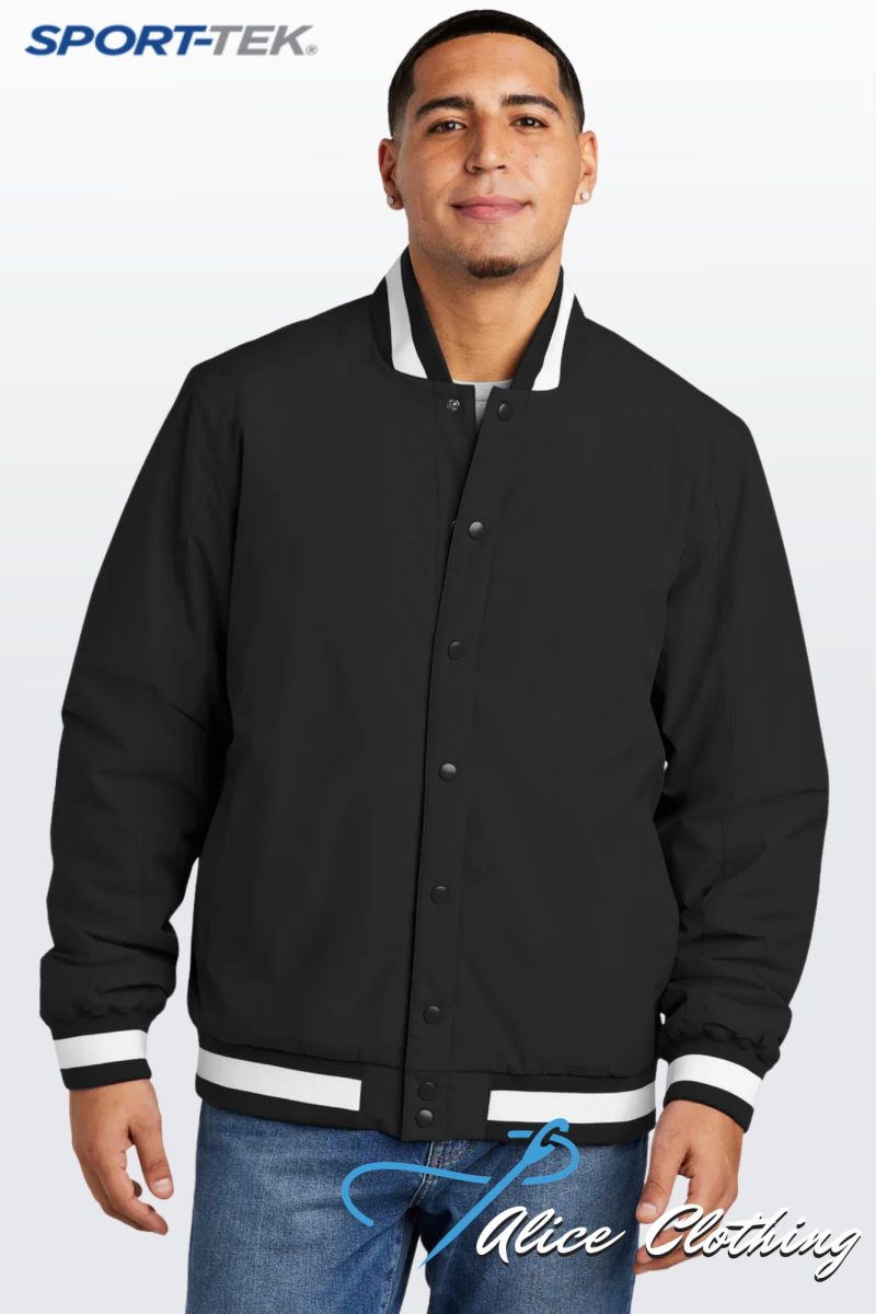 Man wearing a black varsity jacket with white striped cuffs and hem, standing against a light gradient background with SPORT-TEK logo in the corner.