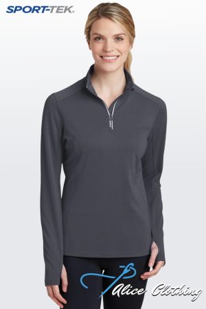 Smiling woman wearing a dark gray quarter-zip athletic top and black leggings with a blue script logo on the thigh; SPORT-TEK logo in the upper left corner.